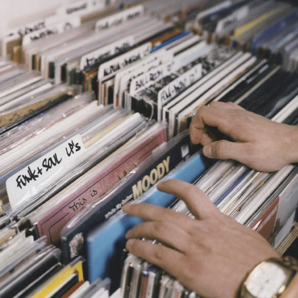 Руки перебирают виниловые пластинки в ряду коробок с ярлыками «Funk + Soul LPs»
