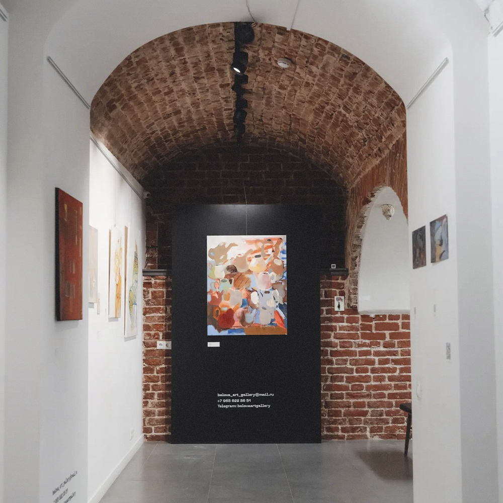 Экспозиция в кирпичном сводчатом зале Belova art gallery: картины на белых стенах и абстрактное полотно на черной перегородке