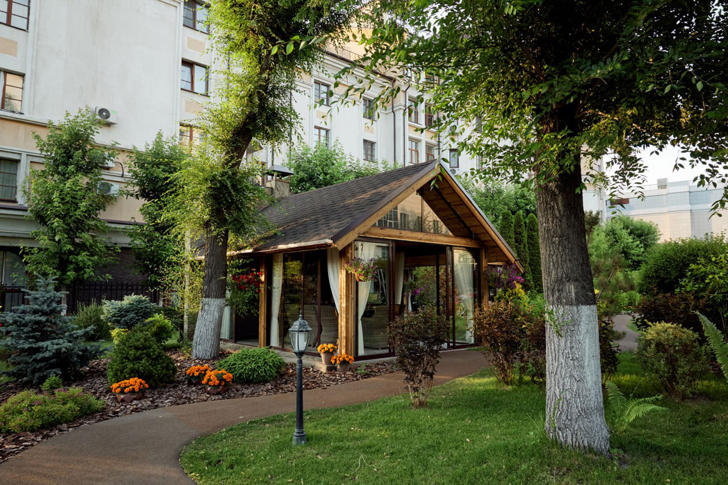 Garden-Cafe Garden Cafe: деревянная веранда со стеклянными стенами среди деревьев и клумб с оранжевыми цветами